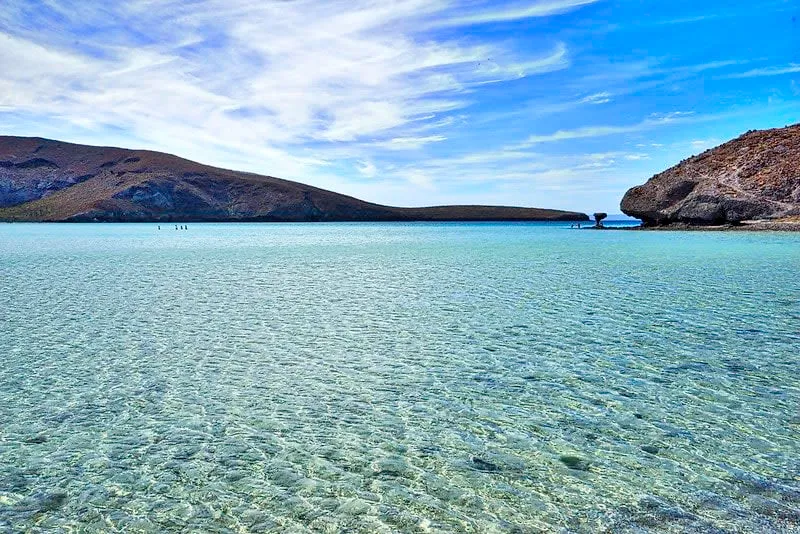 Clear shallow water over rippled sand with low rocky hills behind
