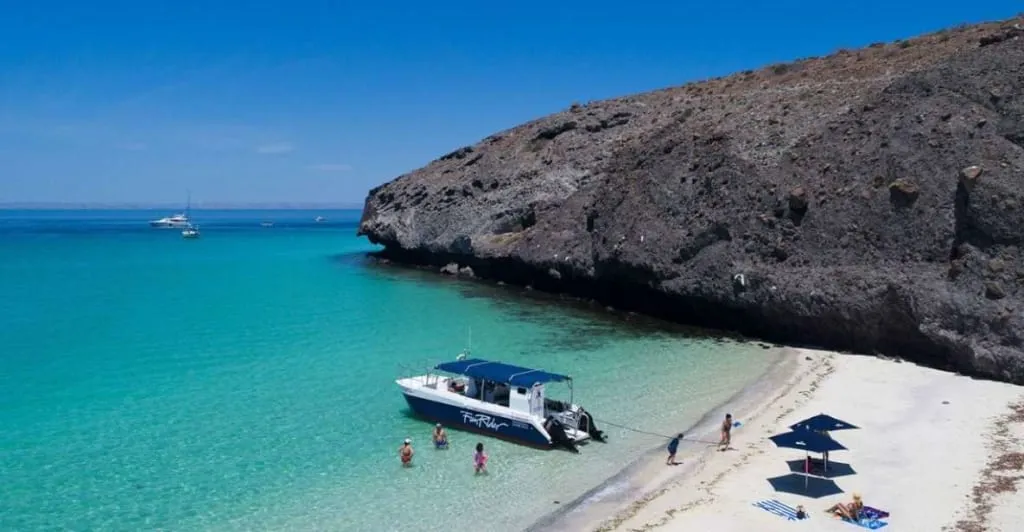 Tour boat floating on bright turquoise water near rocky shore