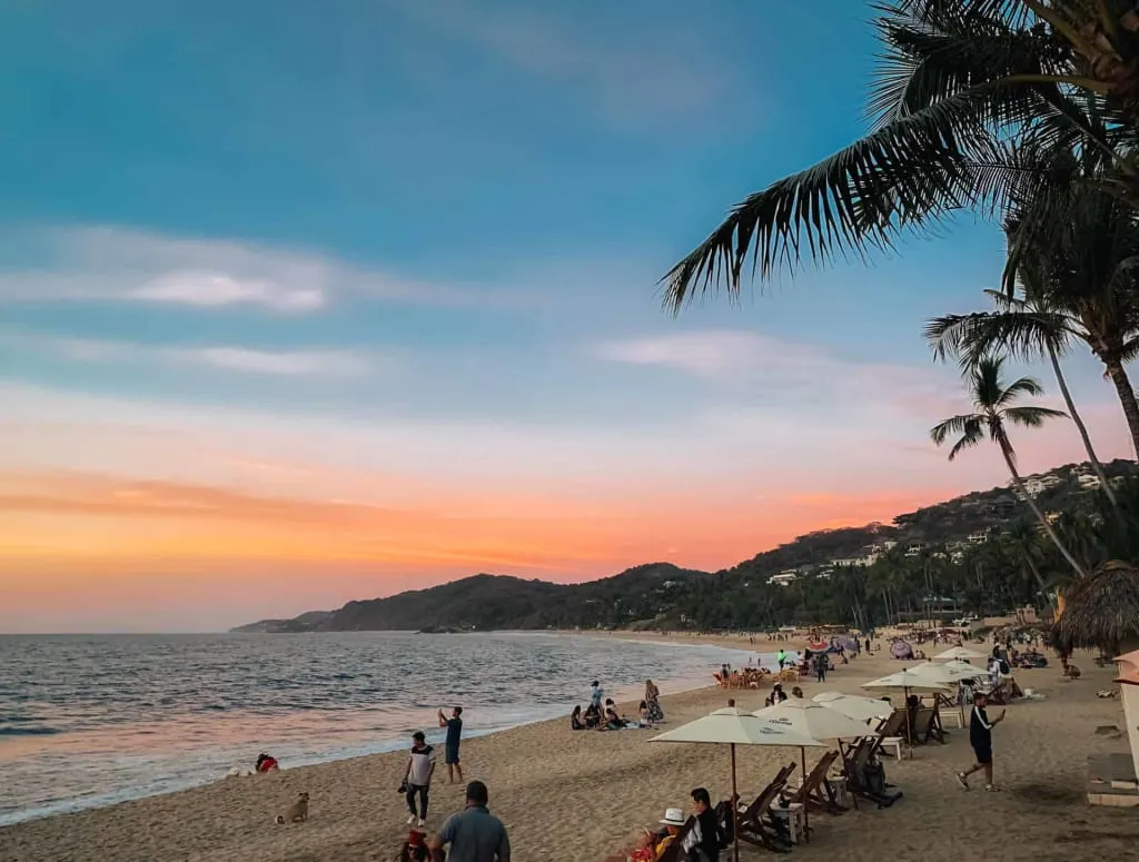 Surfers and beach umbrellas on Sayulita Beach below palm-covered hills