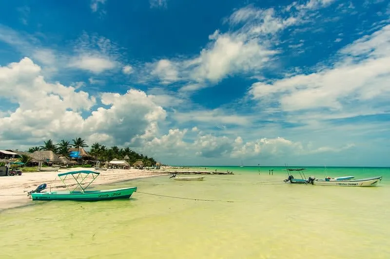Golf carts parked beside white sand and shallow turquoise water on Holbox