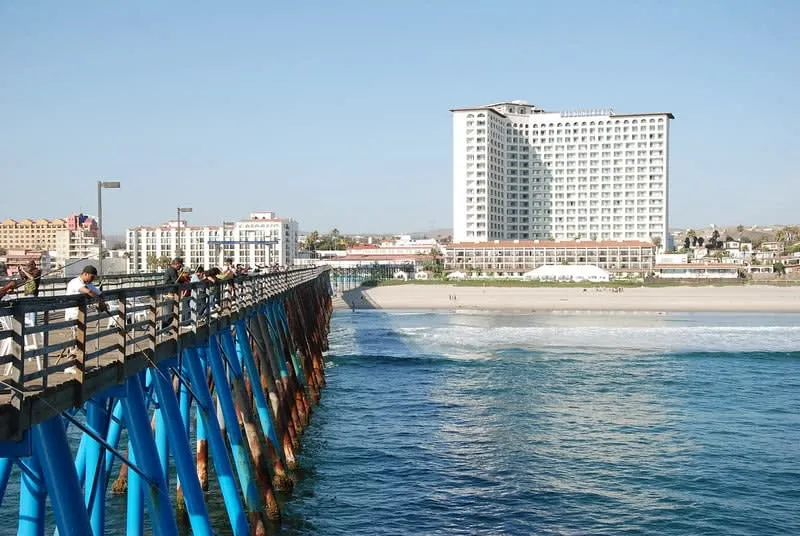 Ocean pier leading toward beachfront hotels under a clear sky