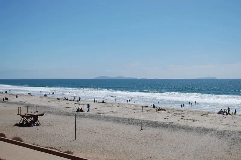 Wide sandy beach with small groups of people walking near the surf