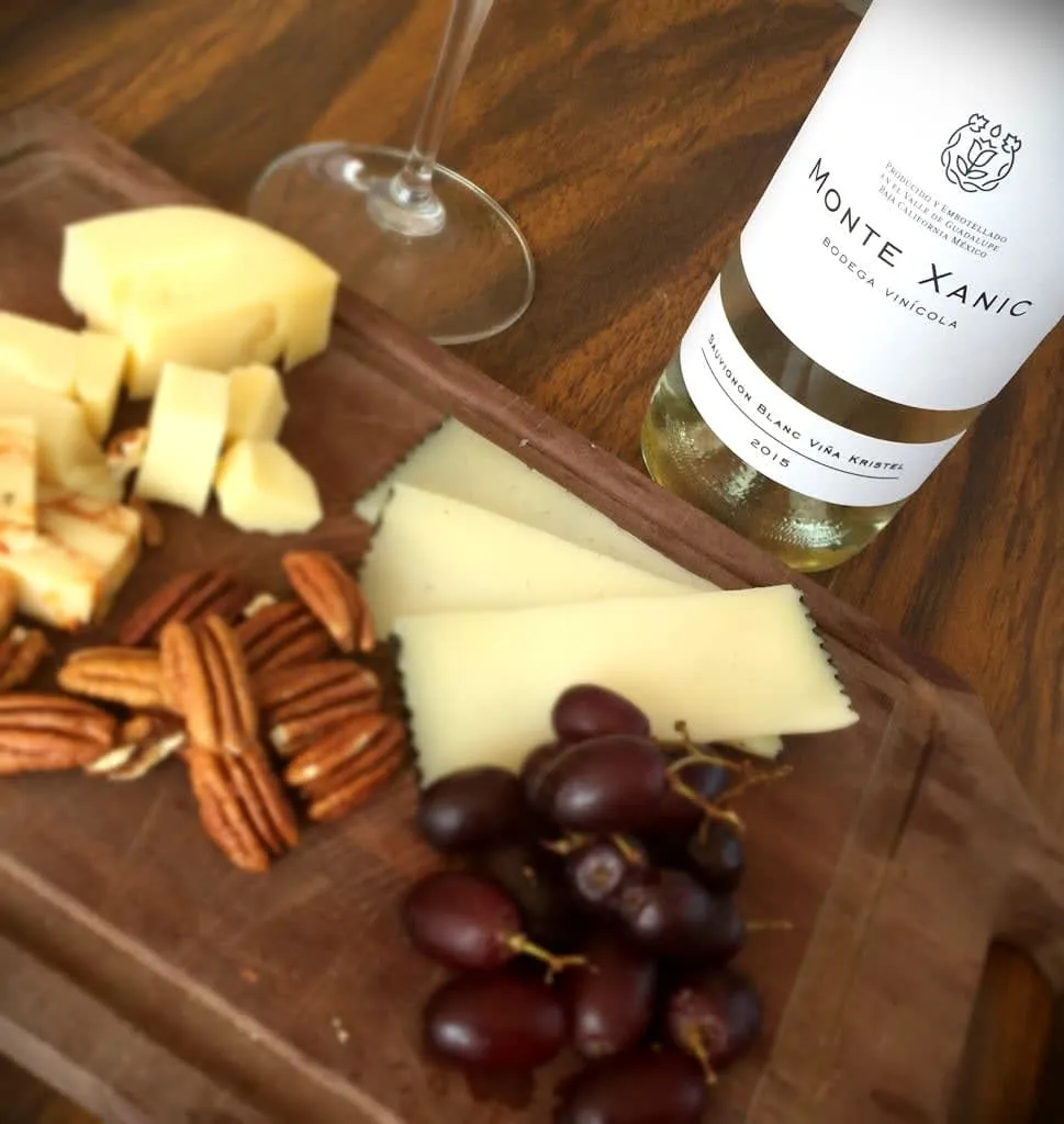 Cheese board with grapes, pecans, and white wine bottle