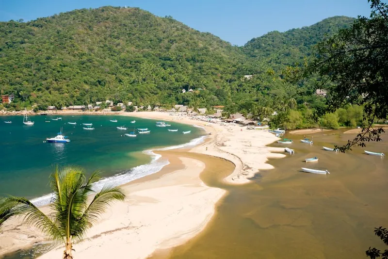 Yelapa beach with green jungle hills and small fishing boats in the bay
