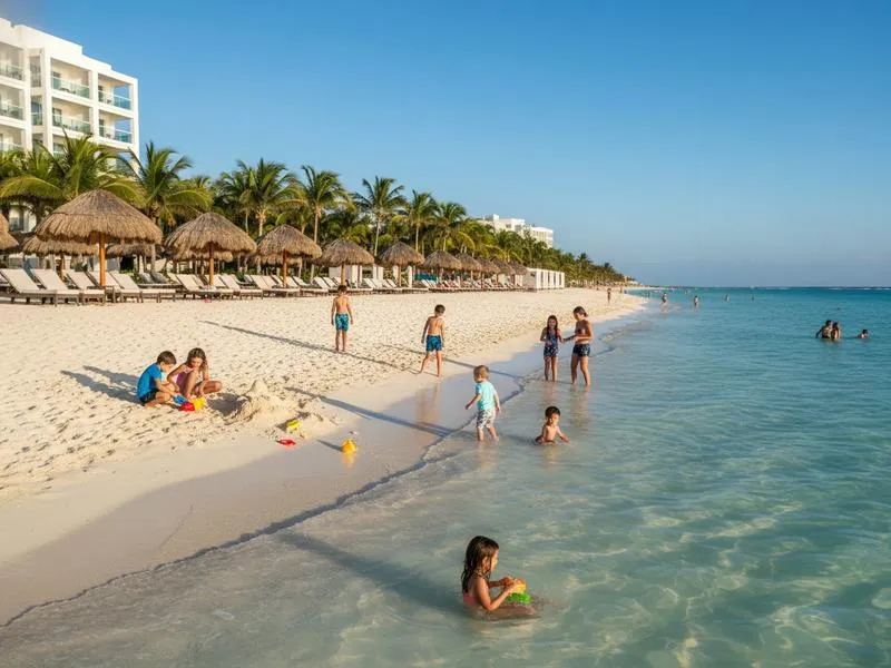 Calm Caribbean beach at a luxury Cancun family resort with shallow turquoise water, sun loungers, and families with children playing in the sand