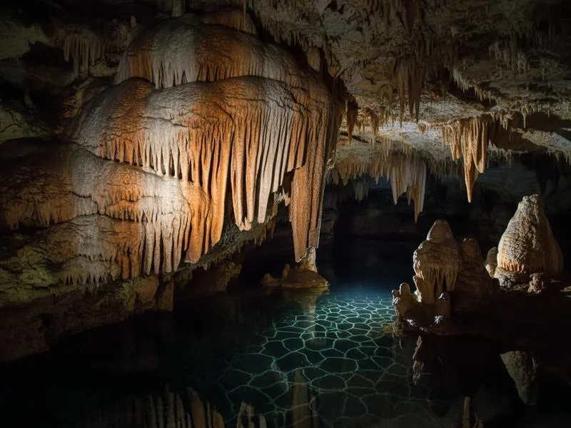 Underground cenote cave with dramatic stalactites hanging from the ceiling and light rays penetrating the crystal-clear blue water below