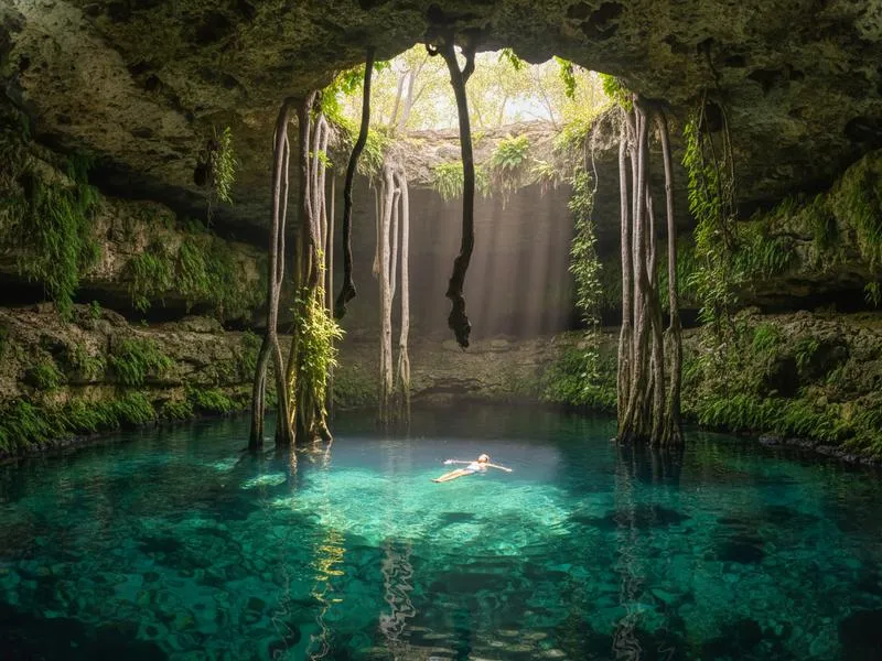 Swimmers in a crystal-clear cenote in Yucatán, Mexico with natural light filtering through