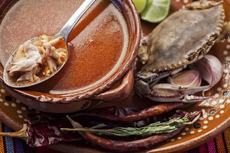 Bowl of finished chilpachole de jaiba — rich red-orange crab soup with whole crab pieces and epazote herb in Veracruz Mexico