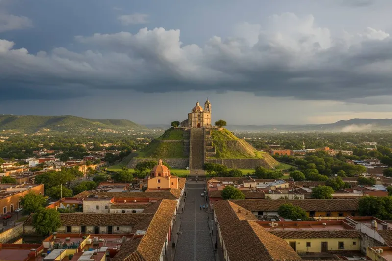 Great Pyramid of Cholula below green rainy-season hills and Puebla Valley church towers