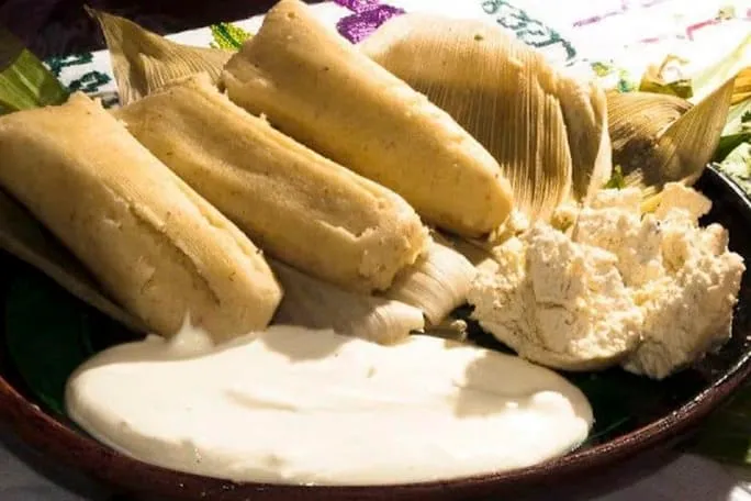Sweet uchepos tamales served in fresh corn husks with sauce and cream