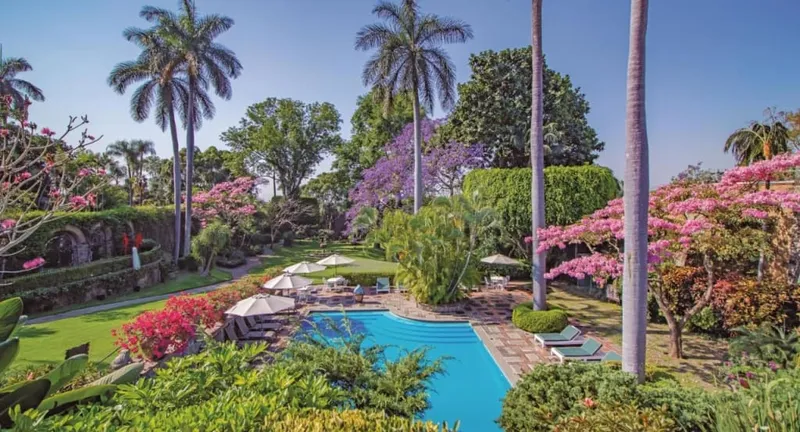 Garden hotel terrace in Cuernavaca with tables, palms, and quiet shade beside a courtyard