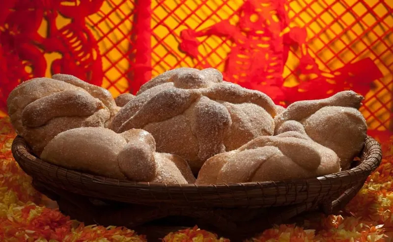 Round pan de muerto bread decorated with bone shapes and orange sugar on a wooden board