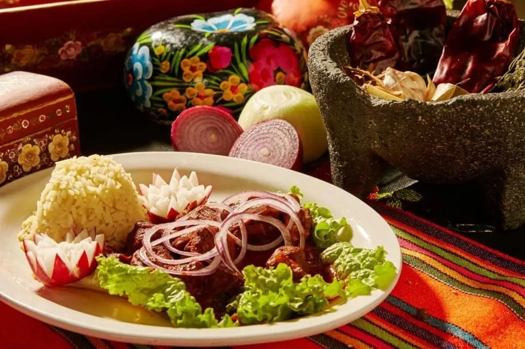 Cochito horneado — slow-roasted pork bathed in ancho chile sauce served with its recado juice, lettuce, and radishes