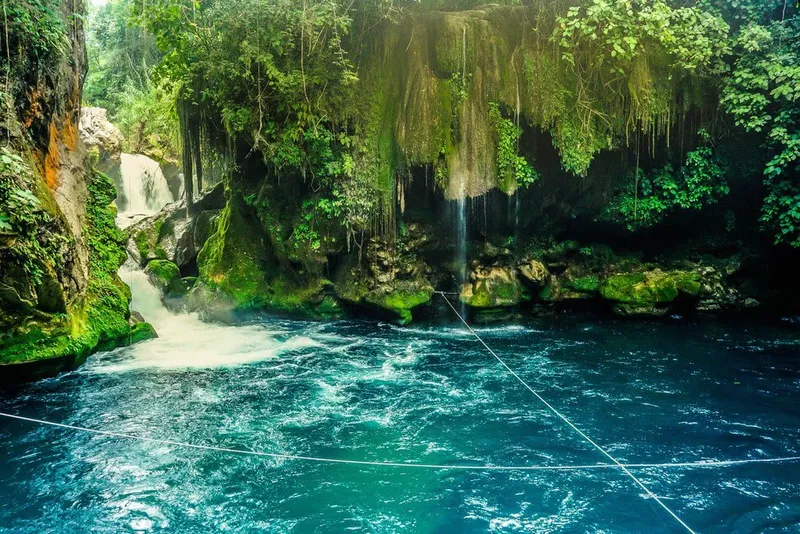 Wide turquoise river in the Huasteca Potosina with jungle banks and layered limestone waterfalls