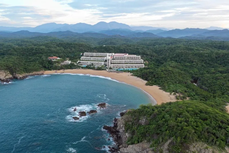 Palm-lined Huatulco beach with calm water and green hills beyond the sand