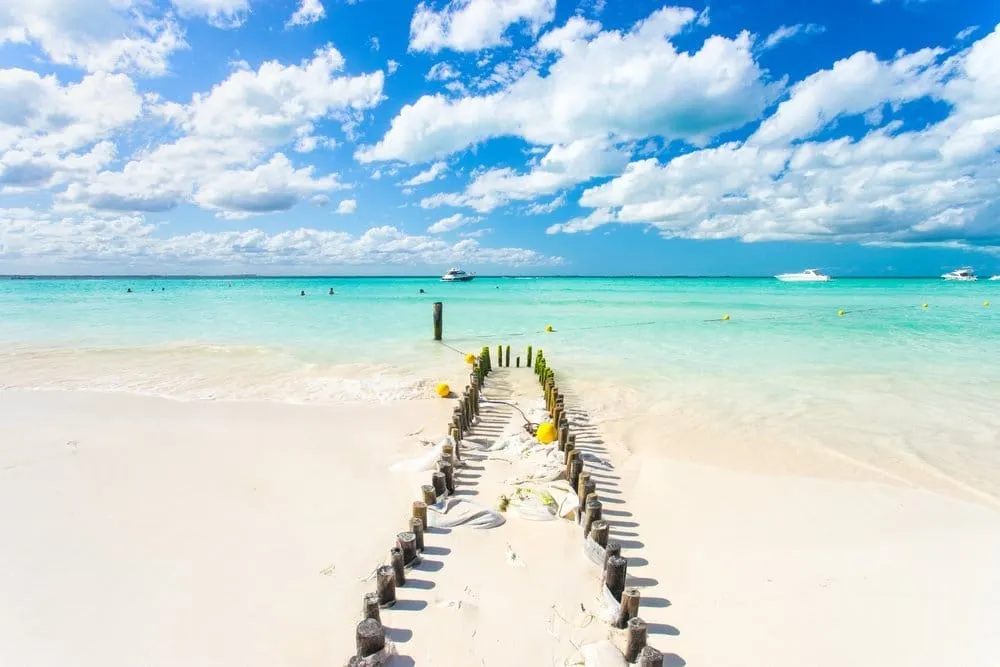 Quiet Isla Mujeres beach with pale sand, shallow blue water, and palm shade