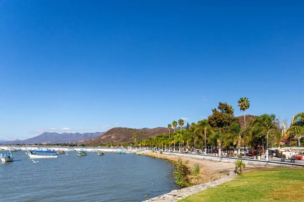 Lake Chapala waterfront at sunset with small fishing boats moored at the malecon pier and the green mountains of the Sierra de Tigre reflected in the calm water