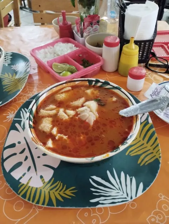 Bowl of red menudo with tripe, hominy, lime, and chopped herbs