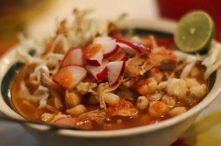 Mexican soup bowls with red menudo and pozole-style garnishes on a table