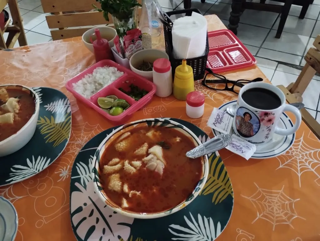 Bowl of menudo soup with tripe, red chile broth, lime, and oregano