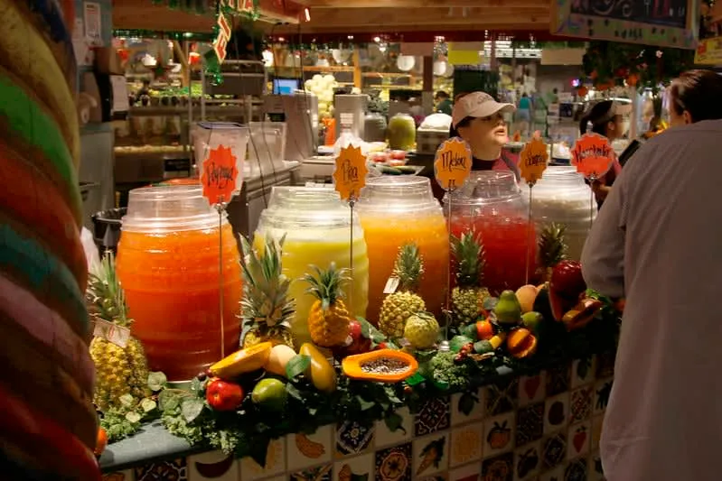 Colorful aguas frescas in large glass barrels at a Mexican market — hibiscus, horchata, and tamarind flavors