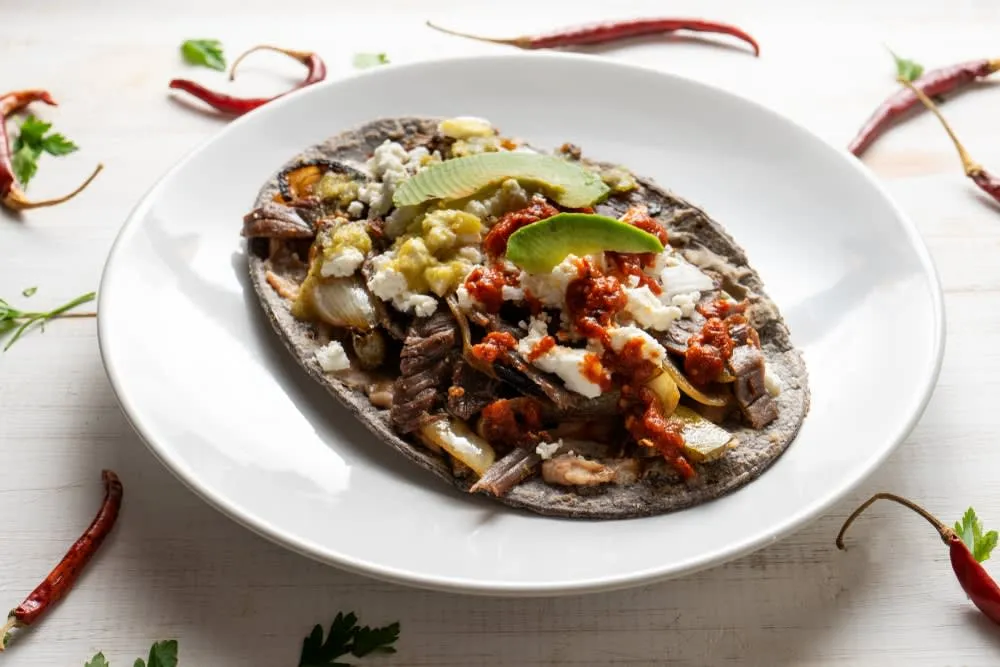 Huarache topped with beans, meat, lettuce, salsa, and cheese