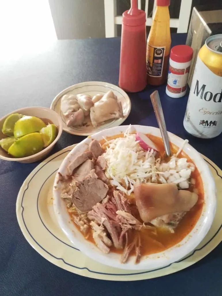 Bowl of red pozole with hominy, radish, lettuce, and lime