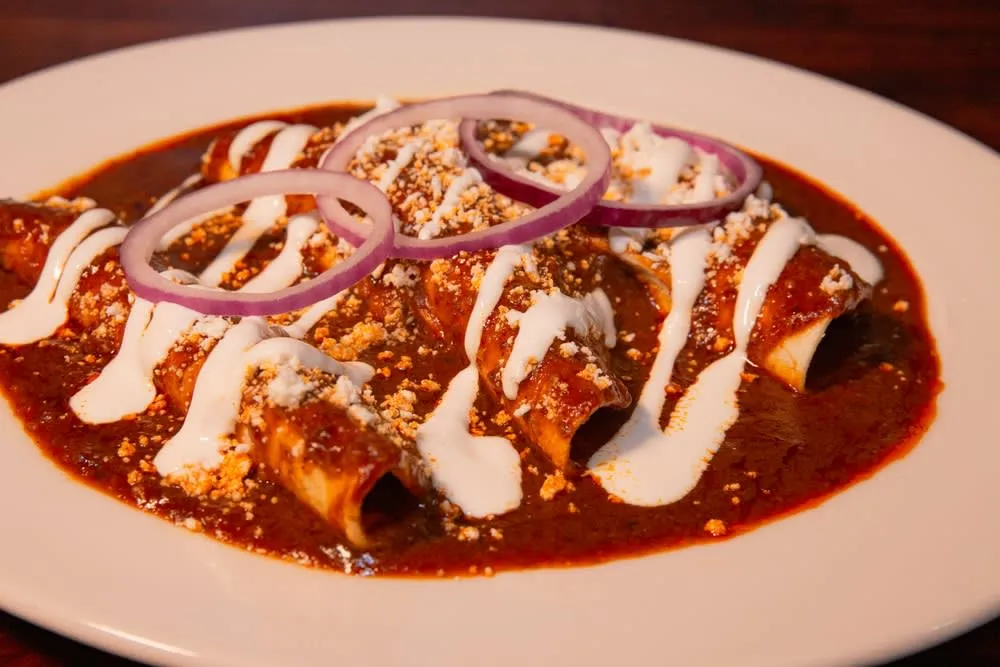 Red enchiladas topped with cheese, lettuce, and crema