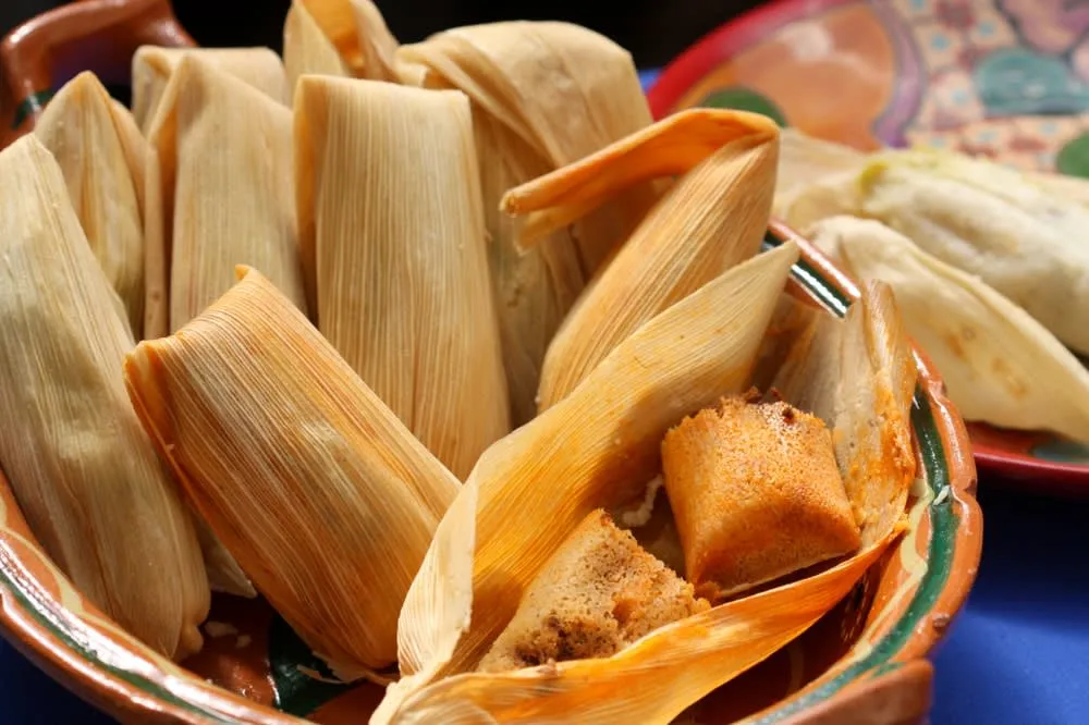Steamed tamales wrapped in corn husks on a serving plate