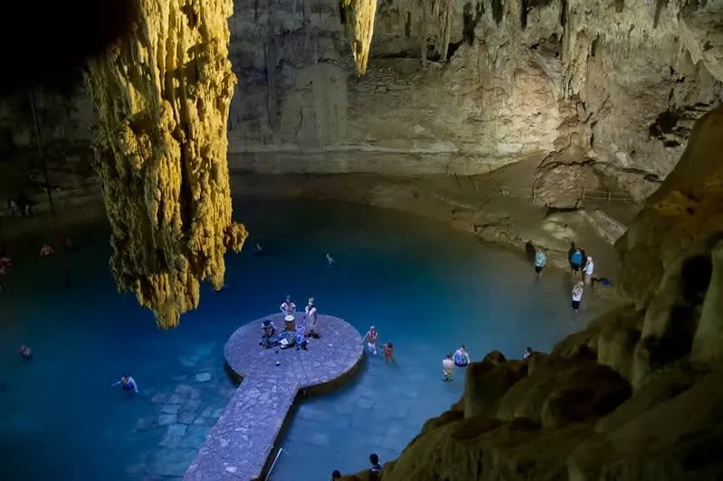 Cenote Suytun near Valladolid — stone walkway extending into crystal water inside a cave with rays of sunlight