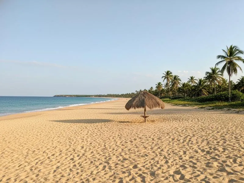 Empty golden beach in Mexico with turquoise water and a single palapa umbrella during low season