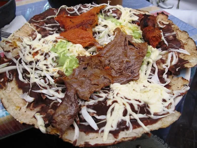 Tlayuda with quesillo (Oaxacan string cheese) and black beans on a comal