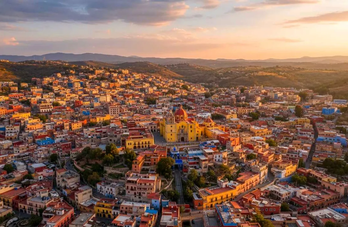 Panoramic aerial view of Guanajuato City's colorful colonial buildings cascading down canyon hillsides under a blue sky