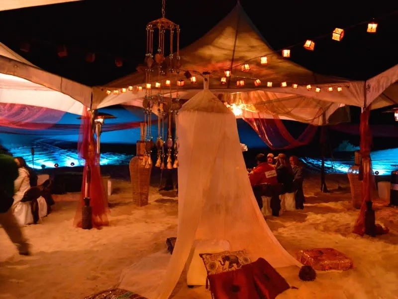 Candlelit desert dinner setup surrounded by pale sand