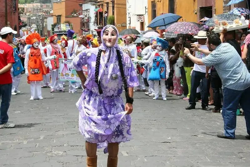 Festival procession in San Miguel de Allende with giant mojigangas (papier-mâché puppets) and crowds on a cobblestone street