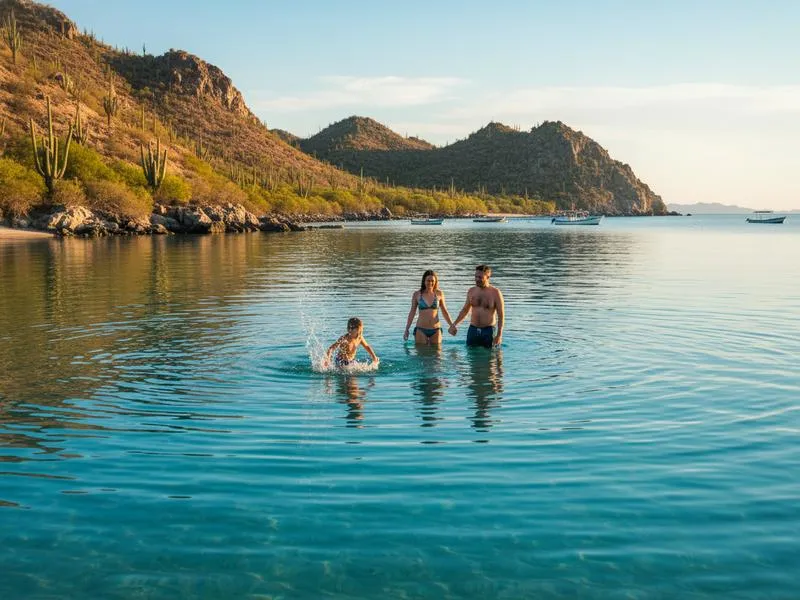 Family enjoying the calm clear waters of the Sea of Cortez at a beach near La Paz in Baja California Sur Mexico, dramatic desert landscape and cactus visible behind them, the water is impossibly blue and calm, children wading safely