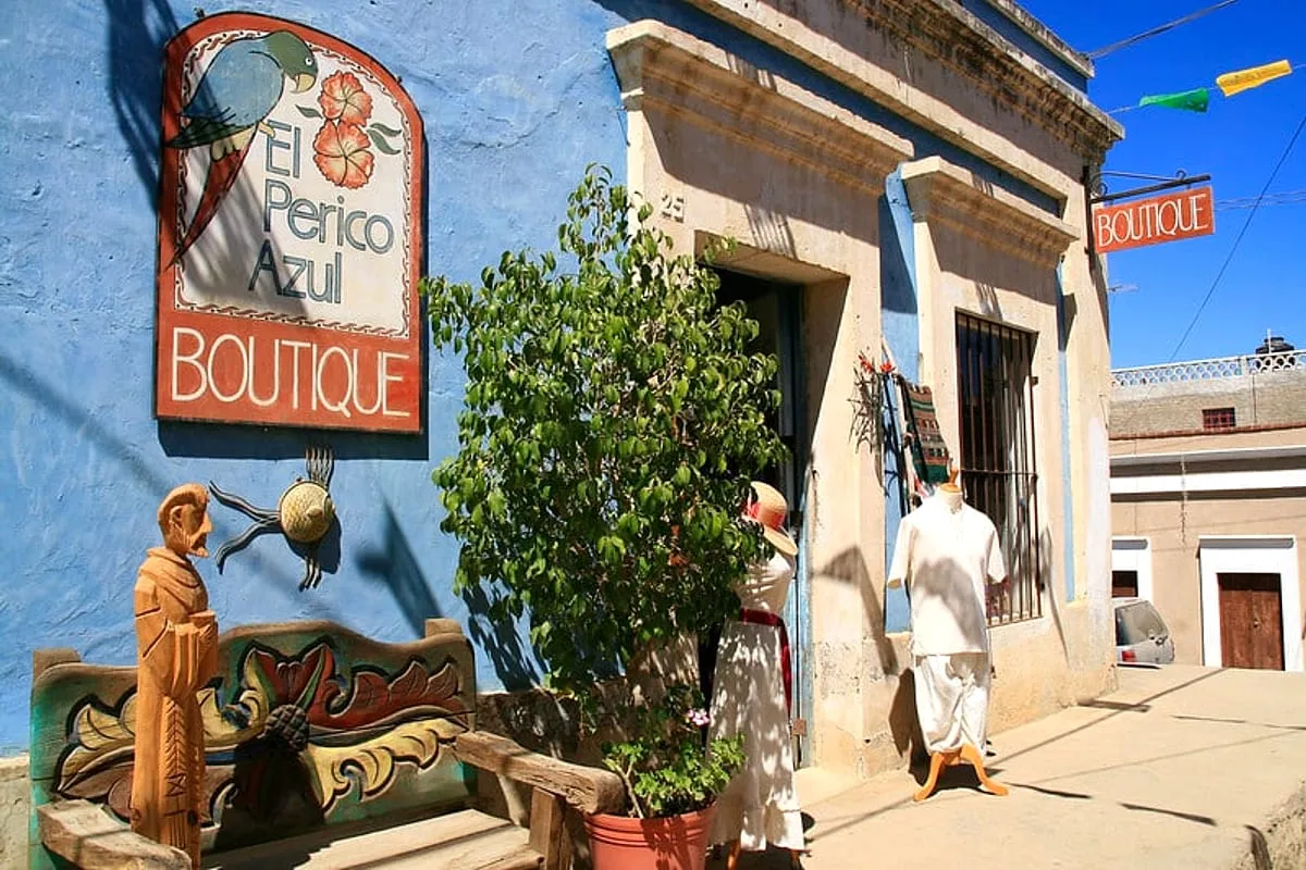 Todos Santos street with colorful Baja buildings, palm trees, and dry hills under summer sun