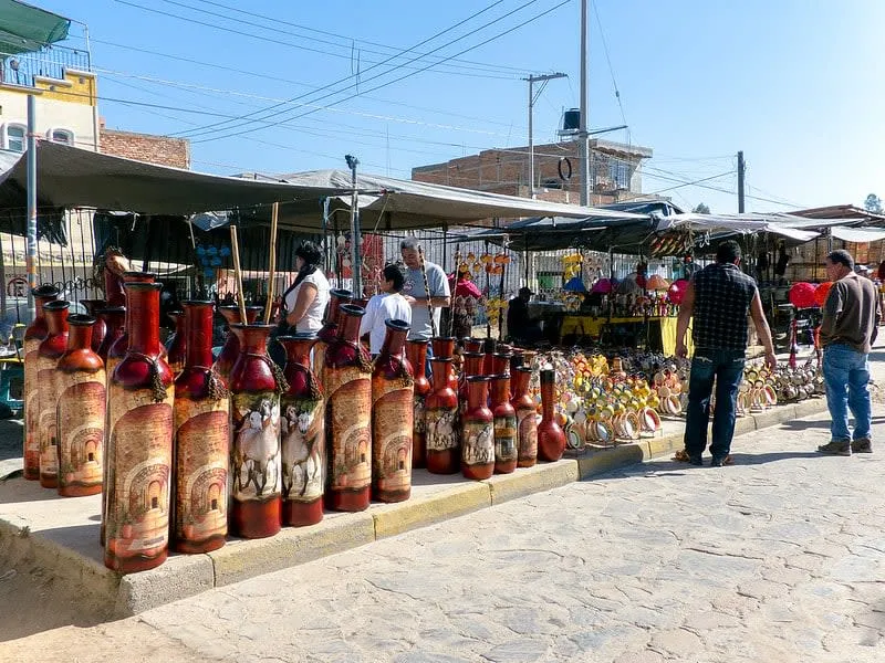 Street market in Tonalá Jalisco on market day with vendors displaying handcrafted pottery, blown glass, and ceramic goods along the main avenue