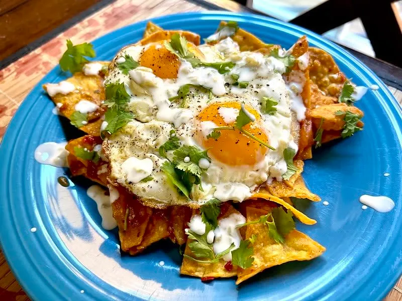 Red chilaquiles topped with cream, cheese, onion, and fried eggs