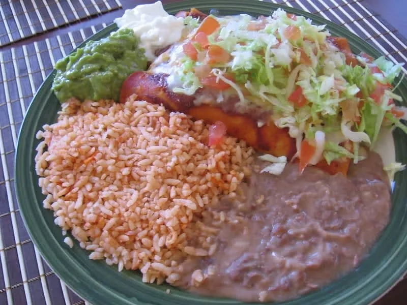 Breakfast enchiladas topped with lettuce, cream, cheese, and sliced onion