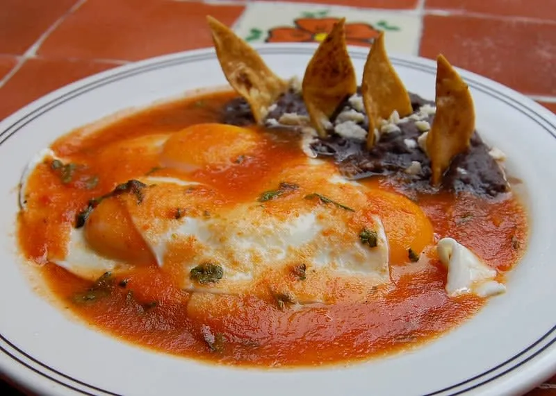 Huevos rancheros with fried eggs, red salsa, tortillas, and beans