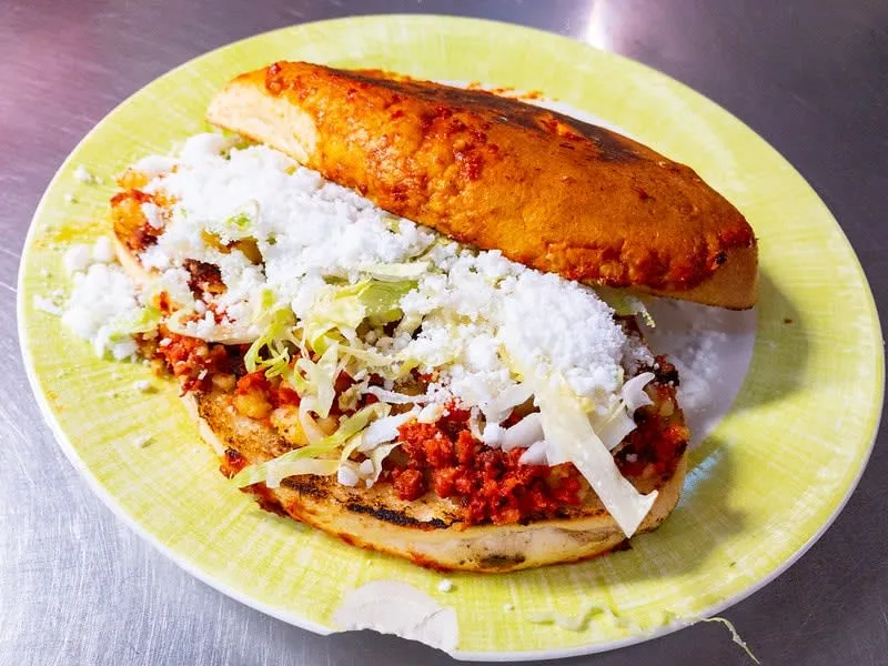 Pambazo sandwich dipped in red chile sauce and filled with potato and chorizo