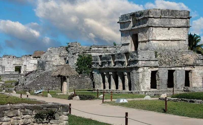 Stone temple and walking paths at the Tulum archaeological site under a cloudy blue sky