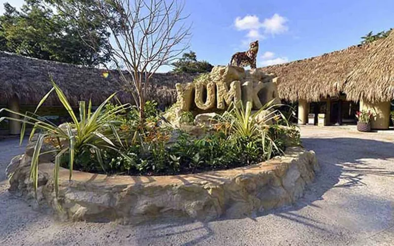 Yumka park entrance with thatched roofs, tropical plants, and a jaguar statue