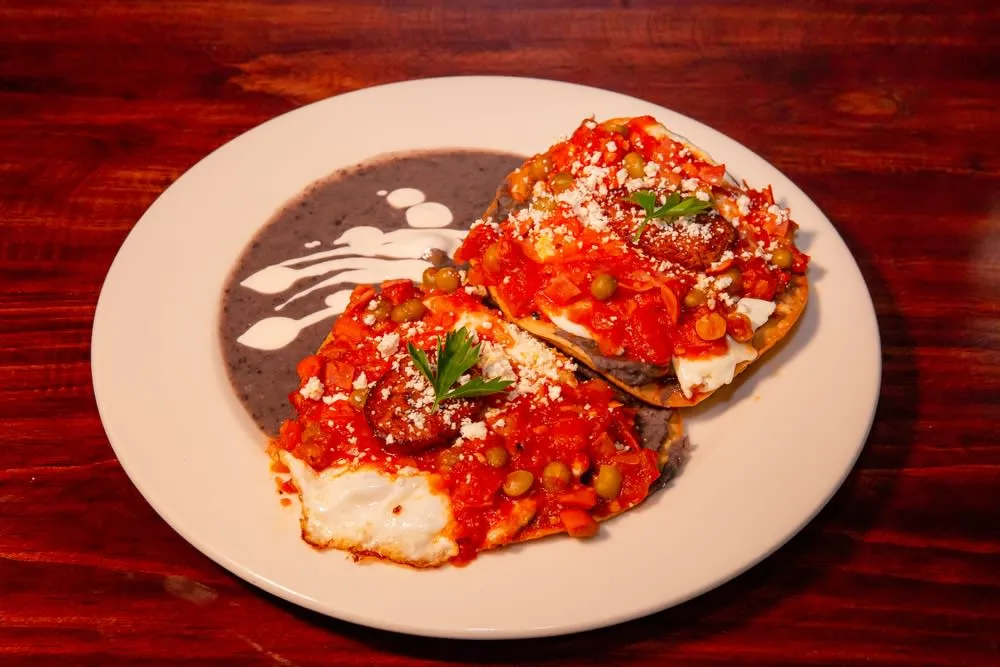 Huevos motulenos — stacked fried eggs on tortilla with black beans, ham, peas, and tomato sauce from Motul Yucatan