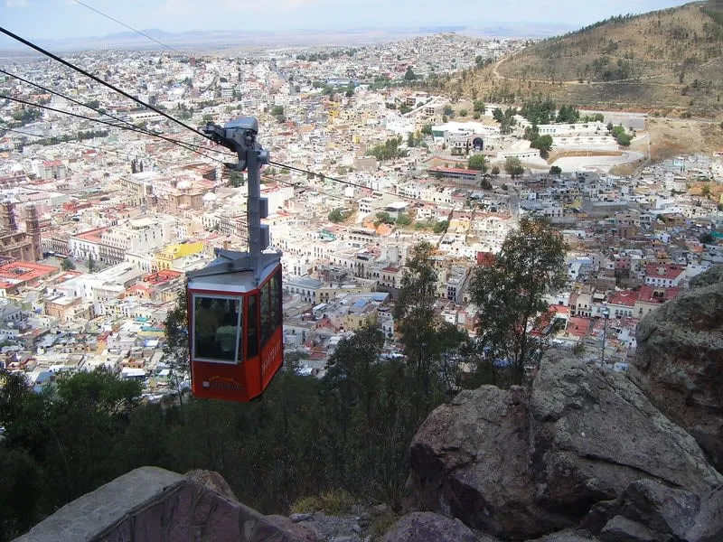 Red cable car crossing above a hillside city