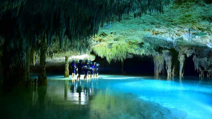 People wading through a flooded cave with stalactites and blue water