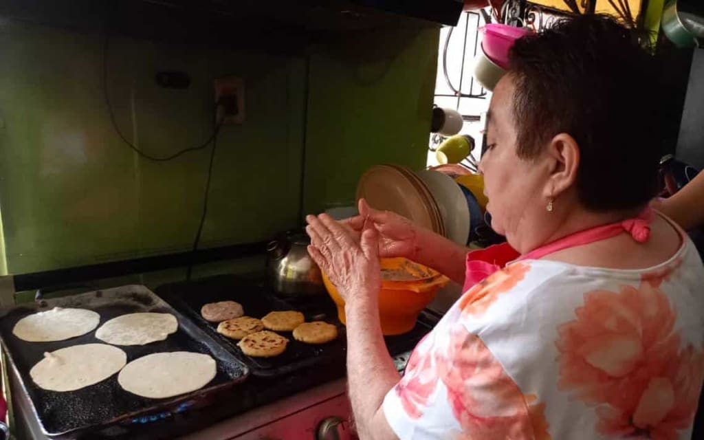 Hands forming bocol masa into round discs before cooking on a comal