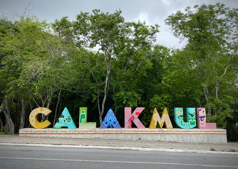 Colorful CALAKMUL letters beside a roadside with green trees behind them