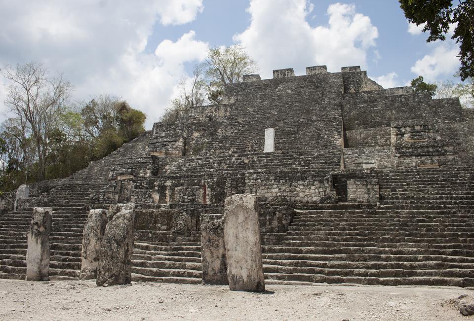 Wide stepped stone ruin with several upright stone slabs in front under a partly cloudy sky